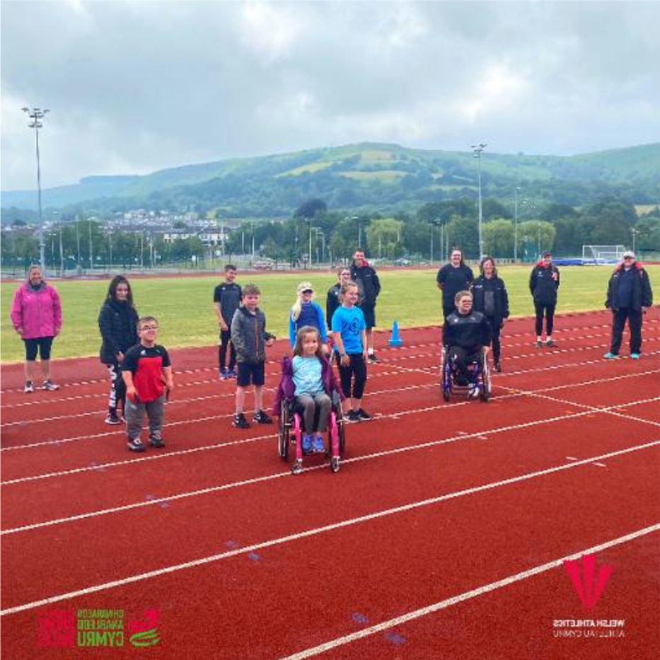 Children and families on an athletics track, including a young wheelchair athlete, at a Sport Ability session