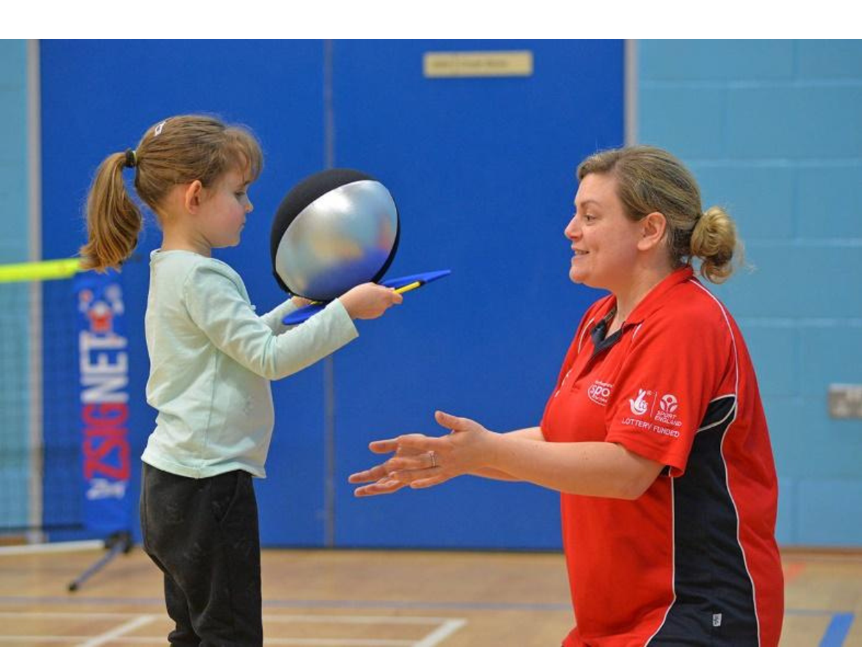 A coach guiding a young child catching a ball during a session